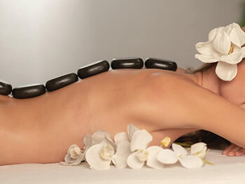 Masaj salonu randevu programı kullanıcısı kadın sırtında spa taşlarıyla yüzüstü uzanıyor.